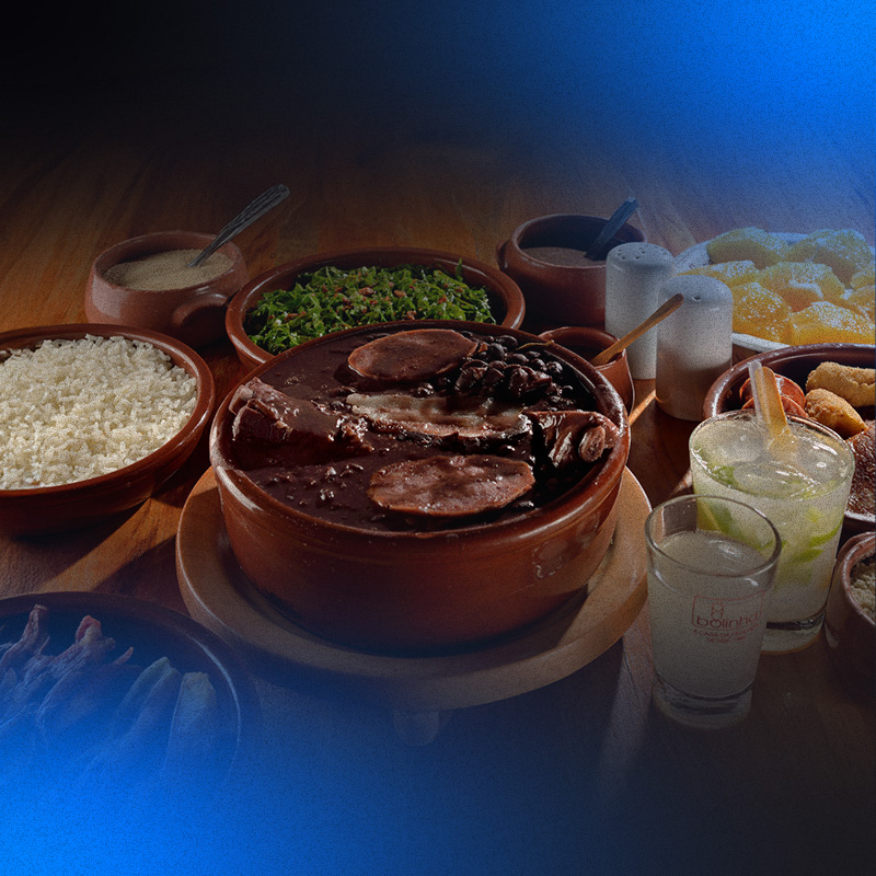 foto de mesa com vários pratos de restaurante a la carte, no centro feijoada, do lado arroz, batata frita