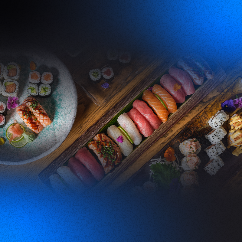 a foto mostra uma mesa com três pratos grandes de formatos diferentes e, em cima deles, diversos tipos de sushi