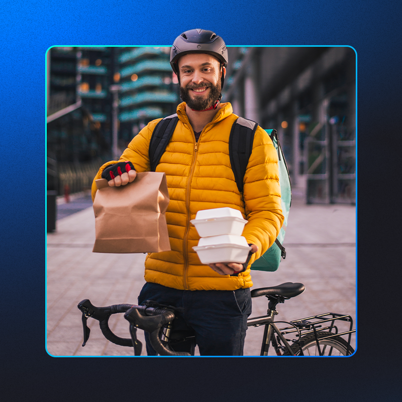 foto mostra entregador de aplicativo de entrega sorrindo enquanto segura a comida que vai fazer delivery