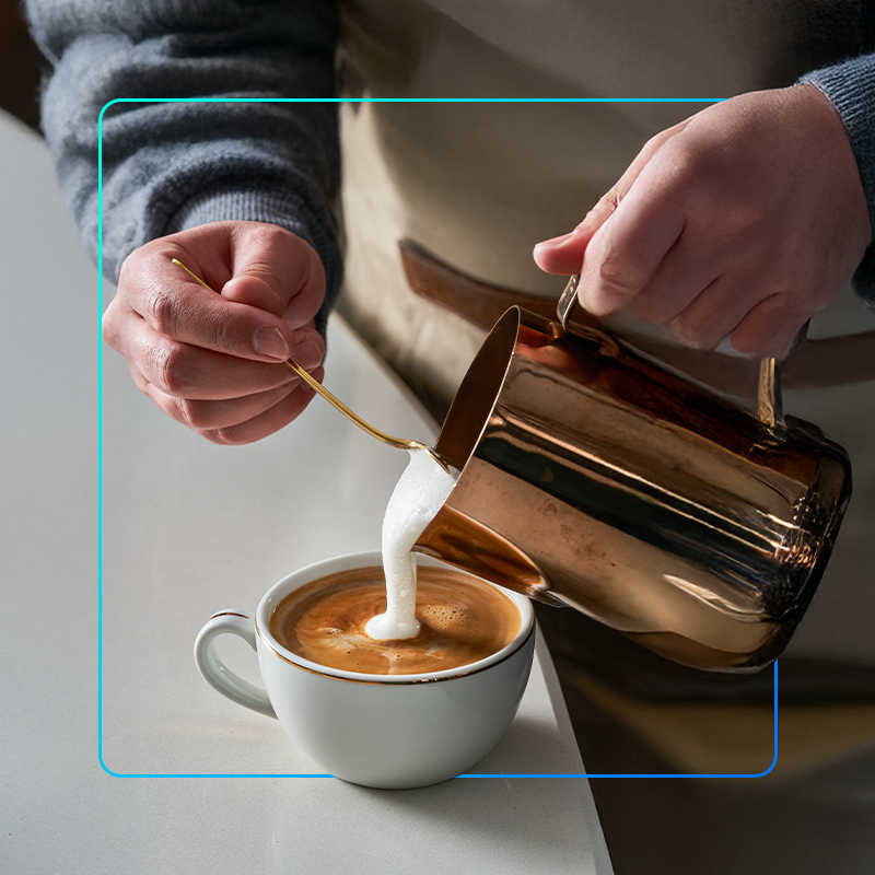 foto mostra uma pessoa fazerndo um latte em franquia de cafeteria